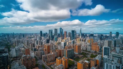 Aerial view of a modern cityscape with high-rise buildings and skyscrapers under a cloudy blue sky, representing urban development and business.