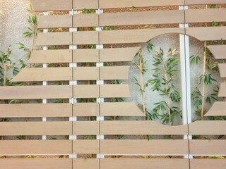 Close-up of geometric wooden slat panels with curved cutouts, showing bamboo stems behind frosted glass for a soft, natural and minimalist interior design accent.