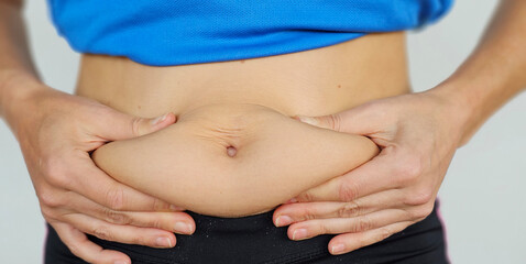 Person Pinching Excess Fat on Their Stomach While Wearing a Blue Shirt and Black Pants