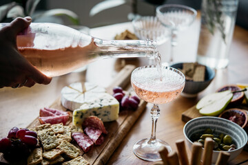 Pouring rose wine with classic snacks of cheese, bread and olives. Party or anniversary celebration.