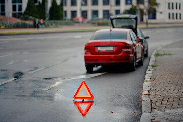 Emergency warning triangle placed behind vehicle after minor rear end collision on wet city road during evening traffic, road safety precautions and hazard signaling for approaching motorists