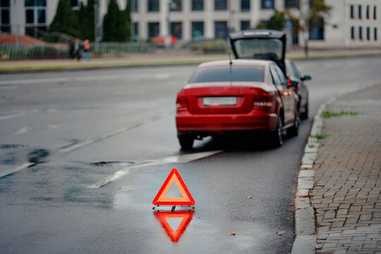 Emergency warning triangle placed behind vehicle after minor rear end collision on wet city road during evening traffic, road safety precautions and hazard signaling for approaching motorists