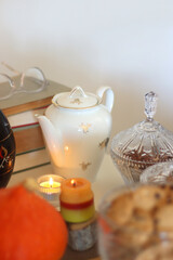 Lit candles, cookies, chocolate, nuts, tea, wine, pumpkins, books, reading glasses and autumn leaves on the table. Autumnal hygge at home. Selective focus.