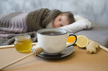 A little girl lies in bed drinking tea with lemon. Concepts of illness, cold, and acute respiratory viral infection.