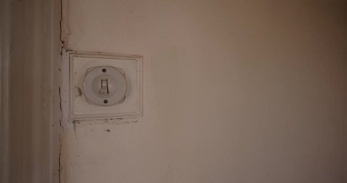 An old fashioned 1940's British house light switch made out of plastic showing a mans hand turning on and off again the electrical vintage switch in an old bedroom or living room.