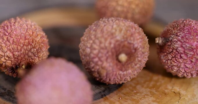 ripe red lychees scattered on a wooden table, ripe lychee fruits,rough textured lychee peel closeup