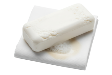 White bar of soap with suds resting on a folded white washcloth on a transparent background