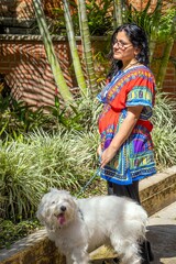 A woman in a colorful dress is walking her white dog