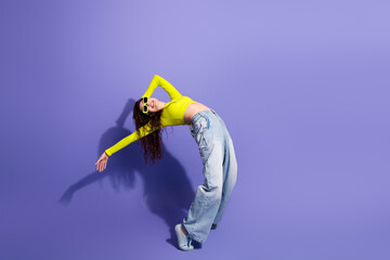 Naklejka premium Young woman in neon yellow top posing and stretching against a purple studio background fashion lifestyle model