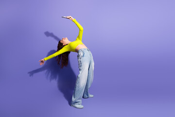 Dancing woman in neon top poses against purple background holding smartphone for a playful fashion lifestyle stock photo