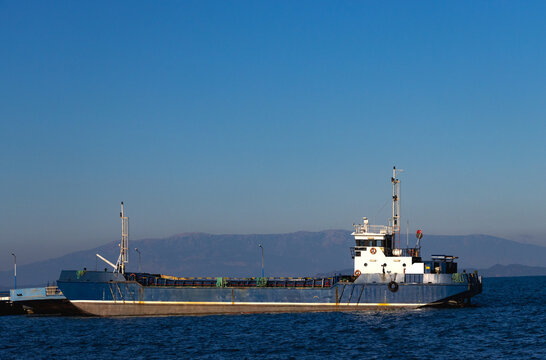 An empty blue cargo ship anchored in port. Foggy skies and calm seas. The theme of maritime transportation and trade.