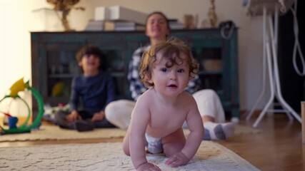 Toddler standing unsteadily in diaper, trying to keep balance while mother supports gently and sibling watches, moment before dropping to crawl, capturing authentic stage of early walking development