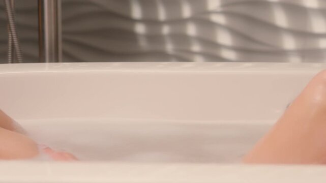 Relaxing happy Caucasian female woman listening audio song in earphones lying in foamy bath girl closed eyes relax enjoying home spa self care bathing in hotel bathtub listening music in headphone