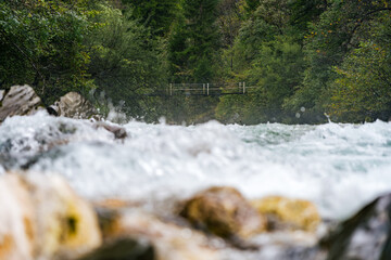 Suspension bridge over the Koritnica River in Slovenia with rushing water in the foreground