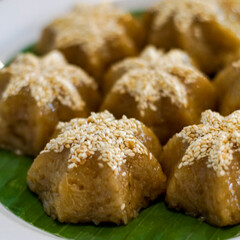 Close-up macro of traditional Asian sweet dessert topped with sesame seeds. Soft lighting and detailed texture highlight its golden glaze, suitable for food photography