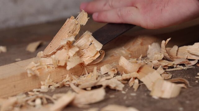 Gros plan sur un menuisier en train de travailler une planche avec un ciseau &agrave; bois dans son atelier.