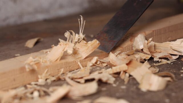 Un menuisier en train de travailler une planche avec un ciseau &agrave; bois dans son atelier.