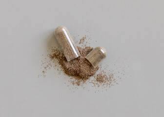 Opened Medical capsule to show brown powder on grey top view. Alternative dietary supplements