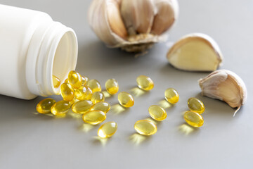 Bottle of yellow garlic oil capsules near whole bulb and cloves on a grey close up. Dietary supplement