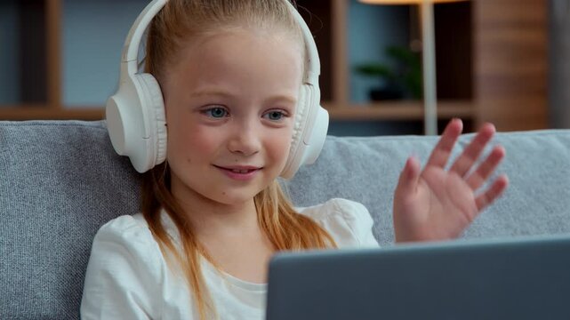 Caucasian happy child little girl talking video call with laptop e-learning greeting hello hi wearing headphones kid daughter with computer talk with online teacher tutor distant education conference