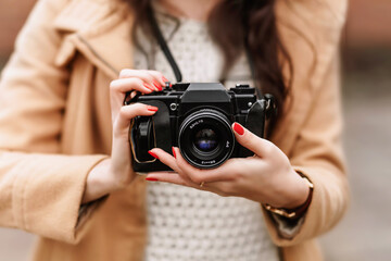 Woman holding vintage film camera outdoors, close-up hands with red nails, analog photography concept.