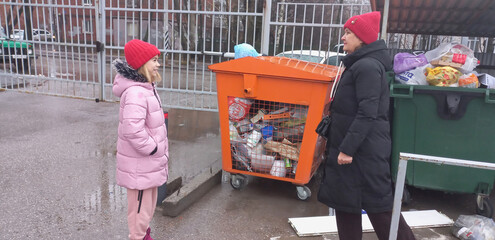 Young girl talking to woman near recycling bin in urban area  