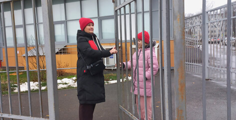 A woman and a girl smile as they open a gate on a street in late autumn.