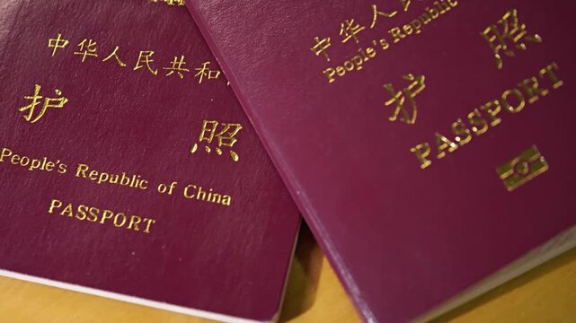 Two deep red People's Republic of China passports are stacked on wood, symbolizing Chinese international travel and border crossing.