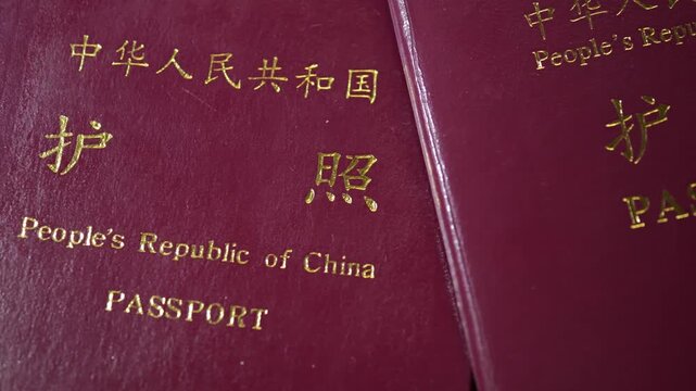 Two deep red People's Republic of China passports are stacked on wood, symbolizing Chinese international travel and border crossing.