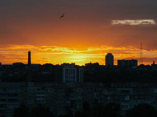 City skyline silhouetted against a vibrant orange and yellow sunset. The dramatic sky creates a stunning backdrop for the urban landscape, with buildings and structures in silhouette