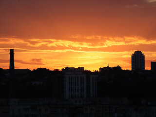City skyline silhouetted against a vibrant orange sunset. The fiery sky casts a warm glow over the city buildings, creating a dramatic and beautiful scene