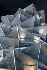 The striking geometric facade of a modern apartment building is illuminated against the dark night...