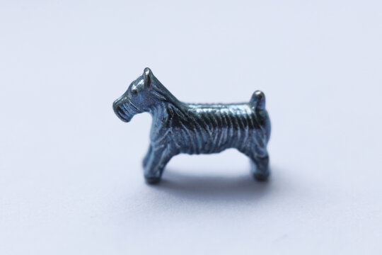 Macro close-up photograph of the iconic metal dog token from the Monopoly board game. Detailed texture, shiny metallic surface, shallow depth of field and selective focus.