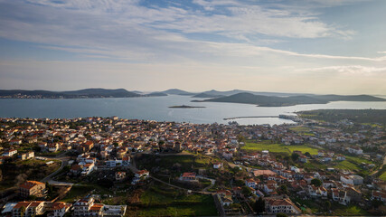 Panoramic aerial view of Cunda Island (Alibey Island) and nearby Aegean islets in Ayvalik, Turkey, showing traditional houses, green fields, harbor, and calm blue sea under soft afternoon light.
