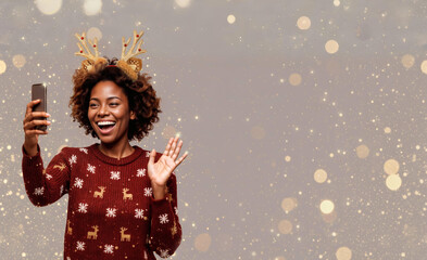 A Black woman with an Afro and reindeer antler headband waves during a video call, wearing a burgundy Christmas sweater. Golden bokeh on light gray creates a festive, cheerful holiday scene.