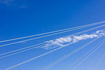 Obraz premium A bright blue sky with wispy clouds, cut by stripes of stretched power lines. Displays a calm and slightly melancholic atmosphere.