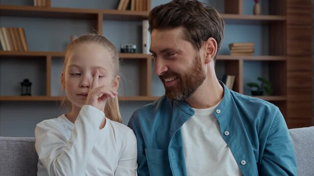 Happy Caucasian family at home father with daughter playing fooling around having fun squint eyes pretend cross-eyed little girl kid child grimacing dad laughing trying funny faces expression laugh