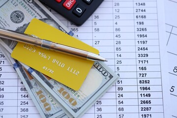 Credit card and pen with US dollar currency money bills banknotes on calculations document background. Business, financial operations and accounting in United States of America