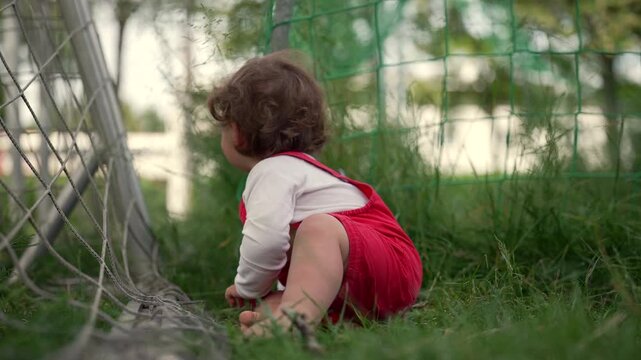 Toddler leaning forward playing with soccer net strings, exploring with intense concentration and curiosity, representing sensory learning and childhood discovery in nature