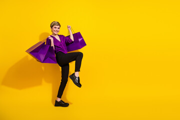 Young woman in a purple blouse jumps with shopping bags against a bright yellow background conveying fashion shopping lifestyle energy and promotional glamour trend style friendly happy sale