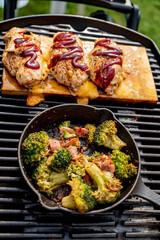 Tender chicken breasts are grilling with barbecue sauce while fresh broccoli cooks in a skillet