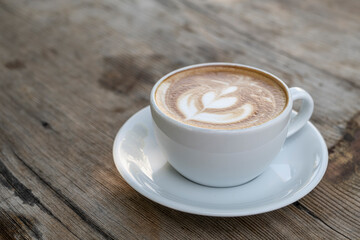 Latte coffee on wooden table. Hot latte cup on rustic wooden surface. Creamy latte coffee on natural wood.