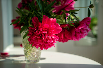Vibrant pink peonies fill a crystal vase on a bright kitchen table, celebrating spring beauty