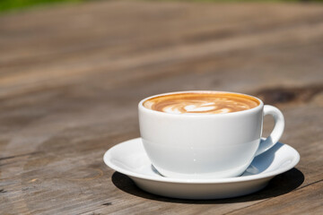 Latte coffee on wooden table. Hot latte cup on rustic wooden surface. Creamy latte coffee on natural wood.
