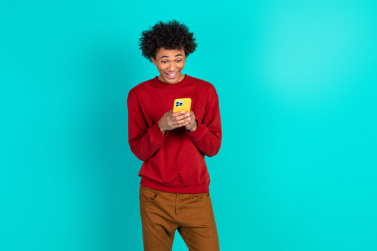 Young man in red sweater using yellow smartphone against teal background smiling and stylish in a casual lifestyle image - Powered by Adobe
