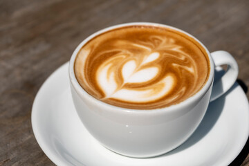 Latte coffee on wooden table. Hot latte cup on rustic wooden surface. Creamy latte coffee on natural wood.