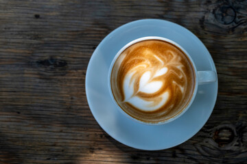 Latte coffee on wooden table. Hot latte cup on rustic wooden surface. Creamy latte coffee on natural wood.