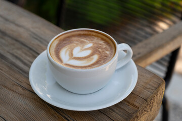 Latte coffee on wooden table. Hot latte cup on rustic wooden surface. Creamy latte coffee on natural wood.