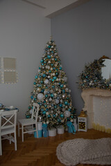 Vertical photo. House room interior with Christmas tree with blue and white bauble, chair, carpet on wood parquet floor, mirror, garland fireplace. Concept of New Year, winter holiday, fun, joy, gift