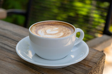 Latte coffee on wooden table. Hot latte cup on rustic wooden surface. Creamy latte coffee on natural wood.